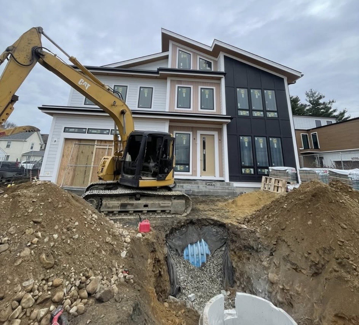 An Oasis jobsite in Newton: a new modern home with an excavator working the lot