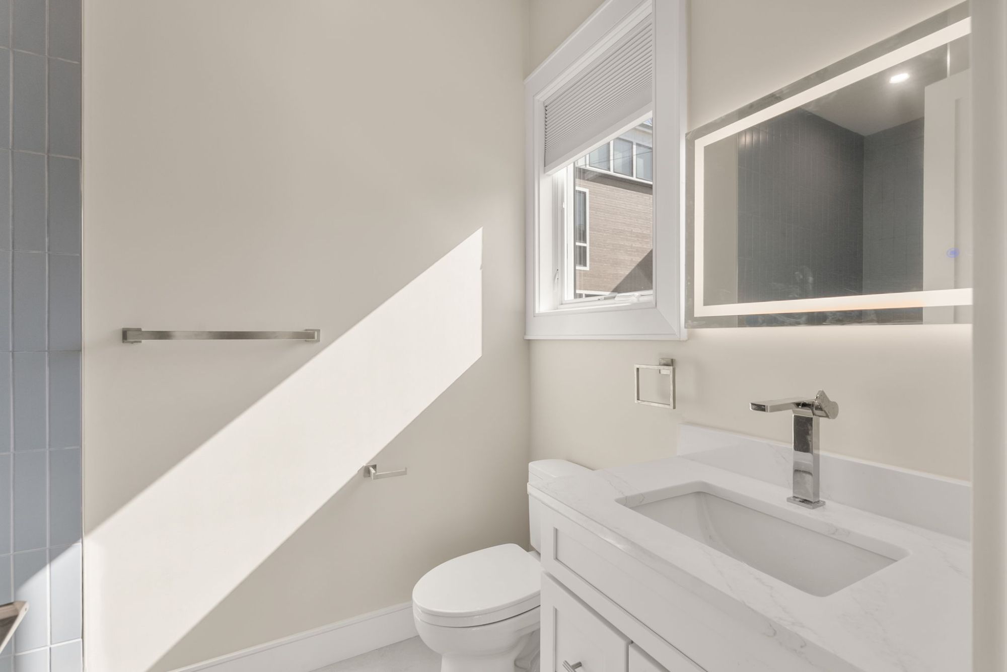 Guest bath with a quartz vanity, lit mirror and tiled shower