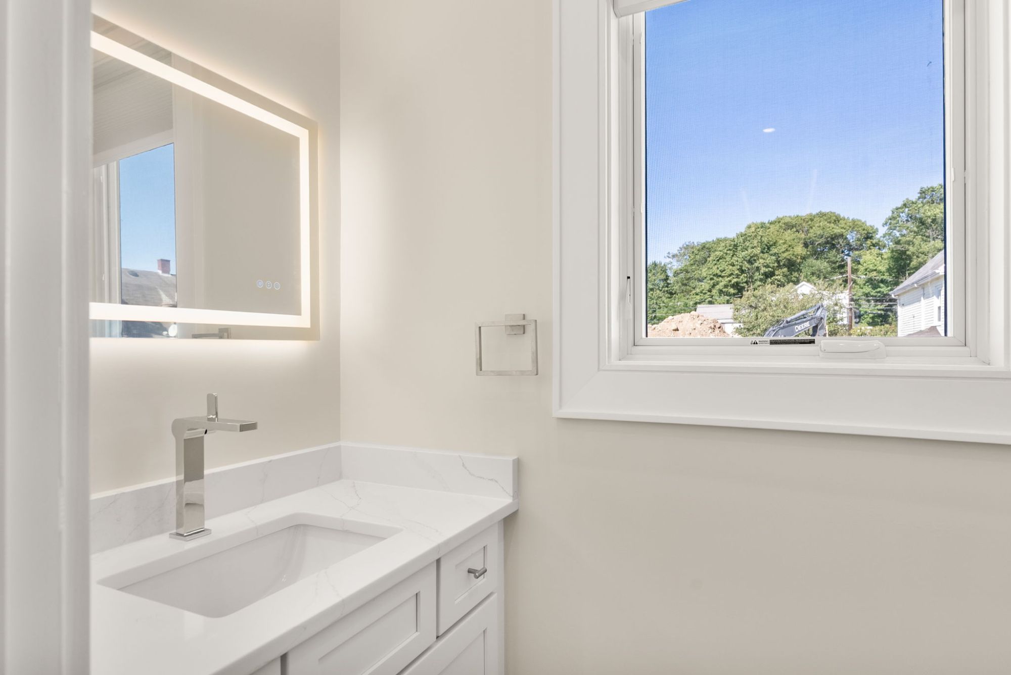 Powder room vanity with a quartz top and lit mirror beside a window